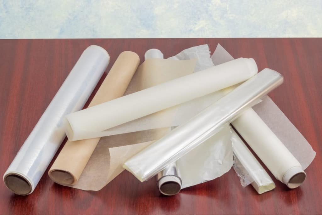 Parchment paper, aluminum foil, wax paper rolls in a line on a wood table