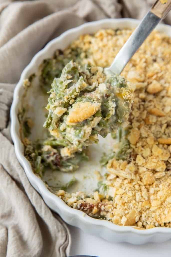 White round casserole dish with half of the green bean casserole gone and a serving spoon taking a scoop