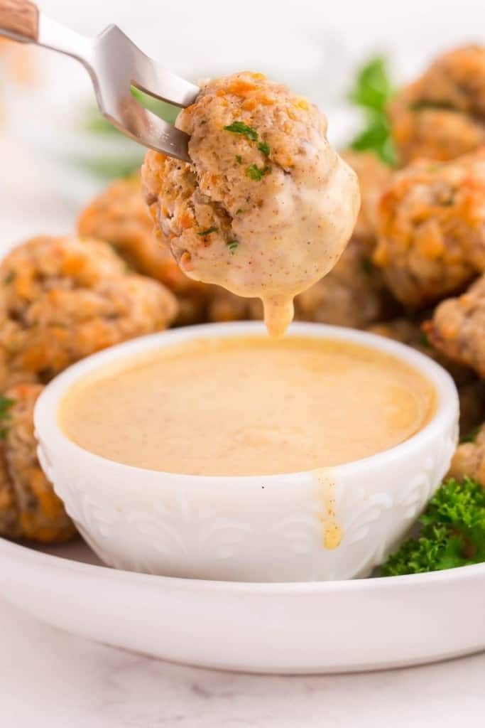 Closeup of sausage balls being dipped into honey mustard sauce