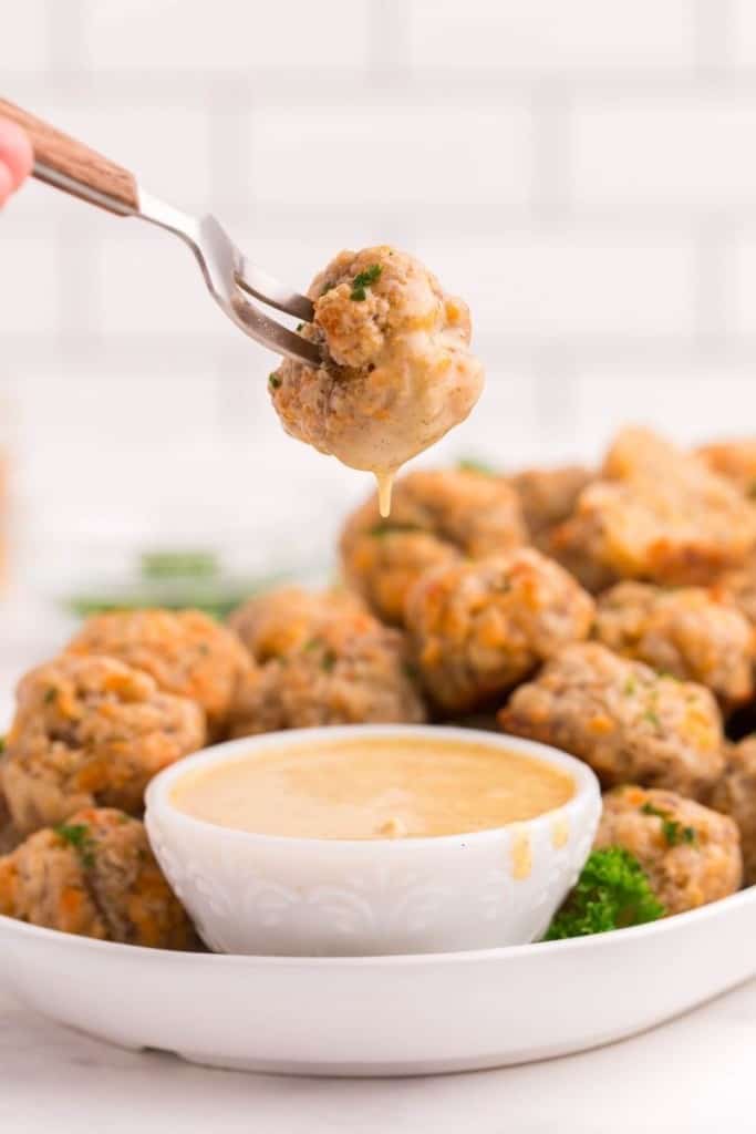 Sausage Balls being dipped in honey mustard on a white serving platter