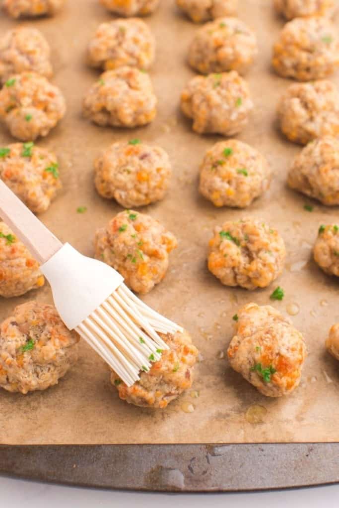 Cooked sausage balls being pasted with butter on a baking sheet
