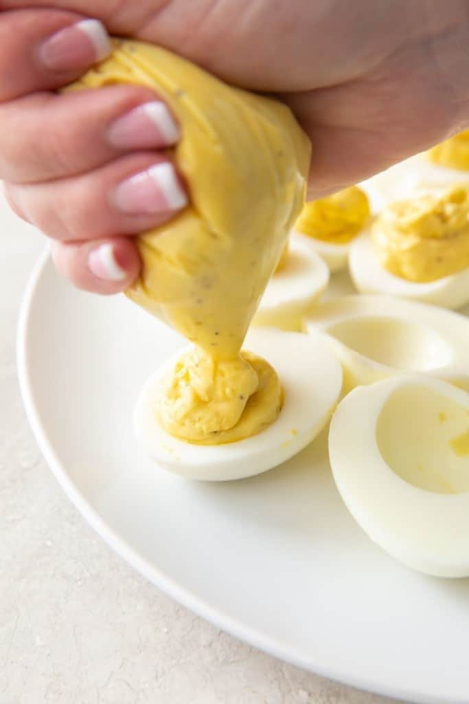 Hard boiled eggs being piped with deviled egg filling