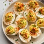 Deviled eggs served on a white round plate and sprinkled with paprika and chives