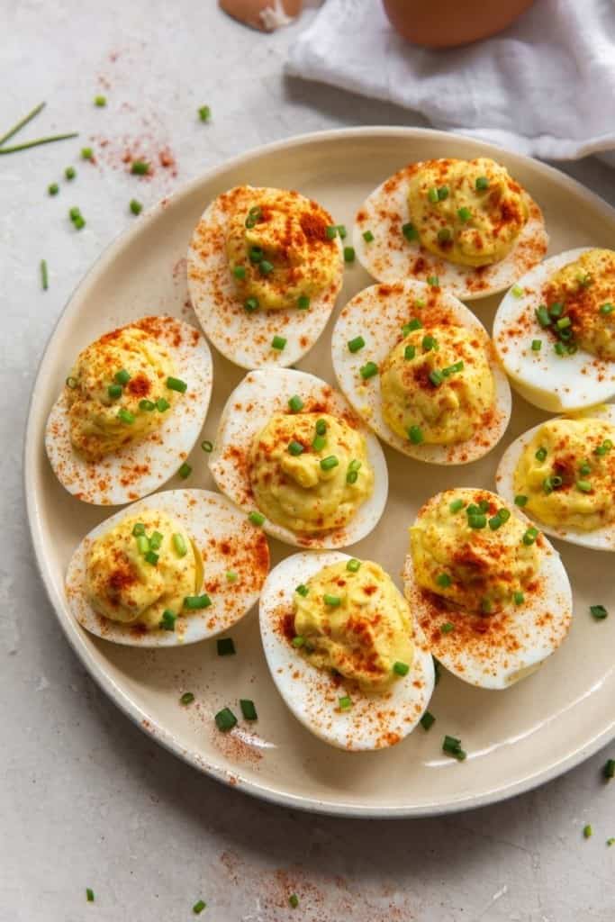 Deviled eggs served on a white round plate and sprinkled with paprika and chives