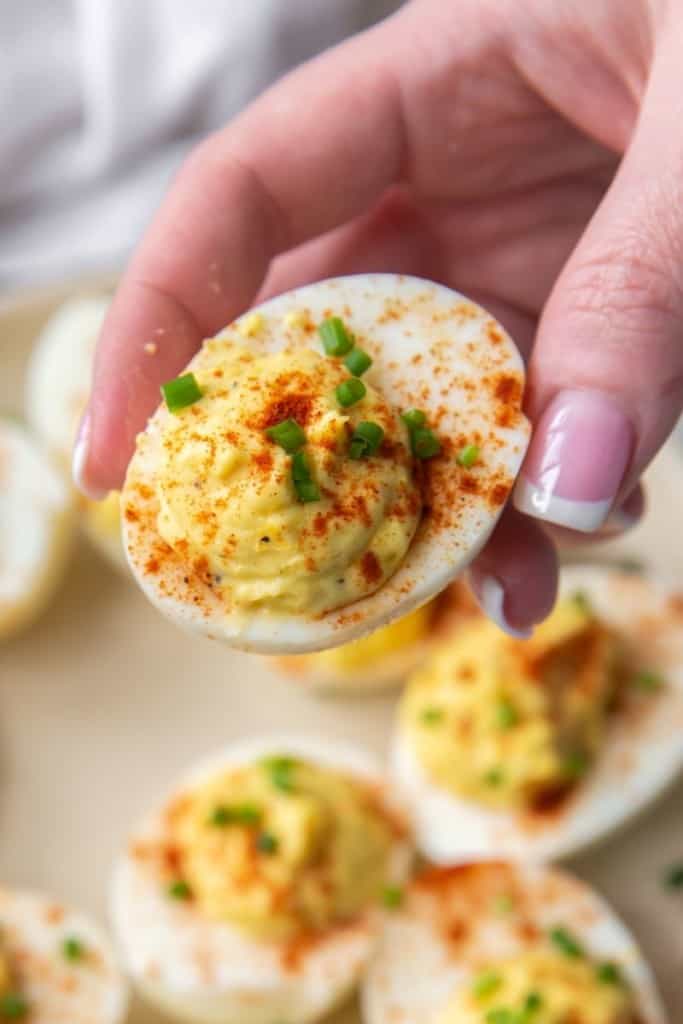 Hand holding deviled egg with no mustard and sprinkled with paprika and chives