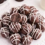 Oreo Balls on a white circular plate drizzled with white chocolate and one bitten into