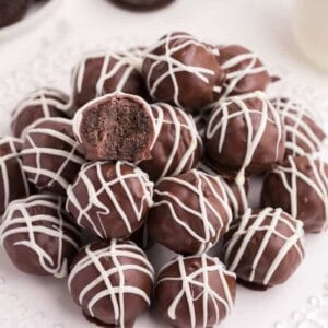 Oreo Balls on a white circular plate drizzled with white chocolate and one bitten into