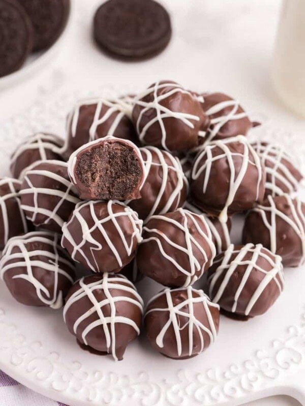 Oreo Balls on a white circular plate drizzled with white chocolate and one bitten into