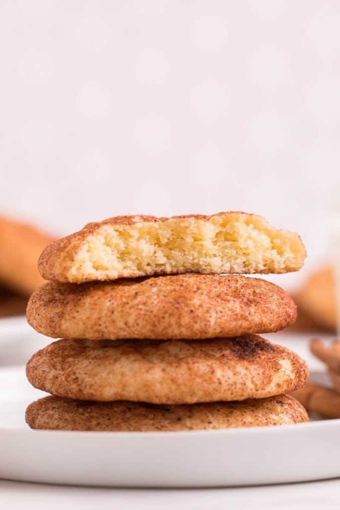 Snickerdoodles stacked on top of each other on a white plate with the top cookie broken in half