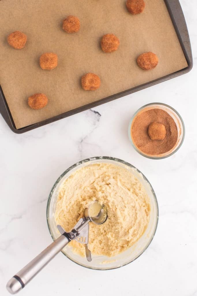 Cookies being scooped and rolled in cinnamon mixture and placed on a baking sheet to cook