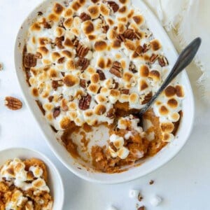 Finished sweet potato casserole with roasted marshmallows and pecans and a serving spoon inside