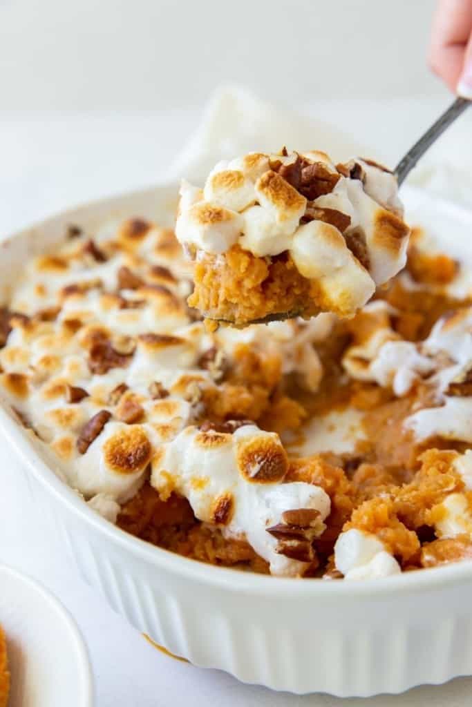 Scoop of sweet potato casserole being held over serving dish