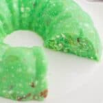 Lime jello salad with cottage cheese on a serving plate with a few pieces missing.