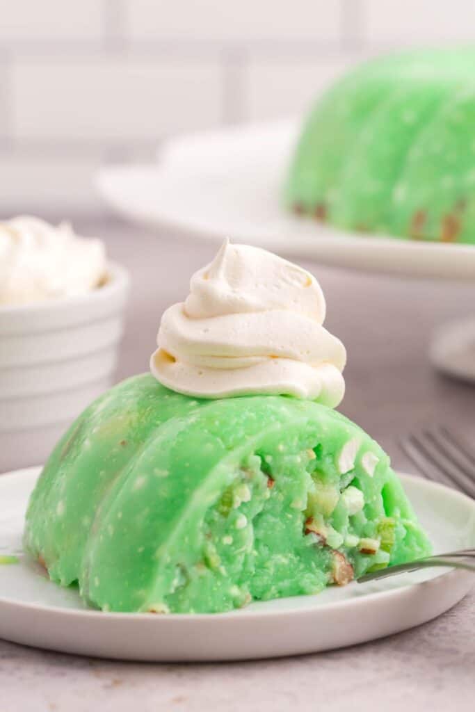 Close up of a piece of lime jello salad with cottage salad with whipped cream on top.