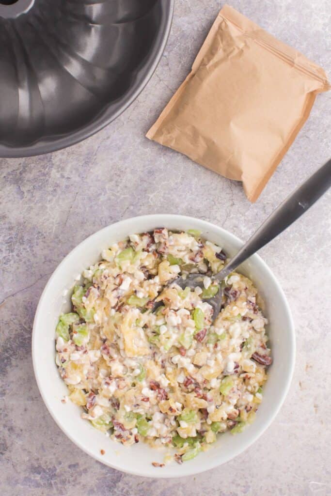 Cottage cheese, celery, pineapple, and pecans being mixed in a bowl to make congealed salad.