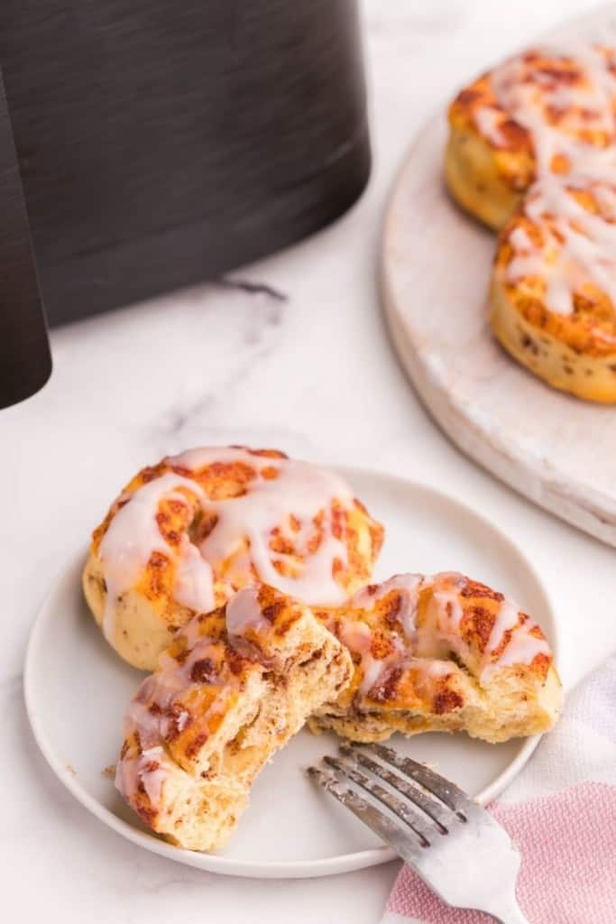 Two cinnamon rolls on a white plate with one cut in half by a fork
