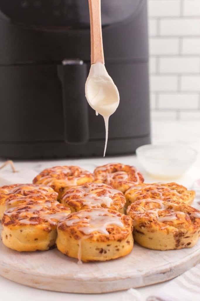Icing being dripped onto cooked cinnamon rolls in front of an air fryer