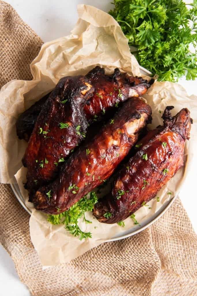 Overshot of air fryer turkey wings on a white plate with brown parchment paper underneath