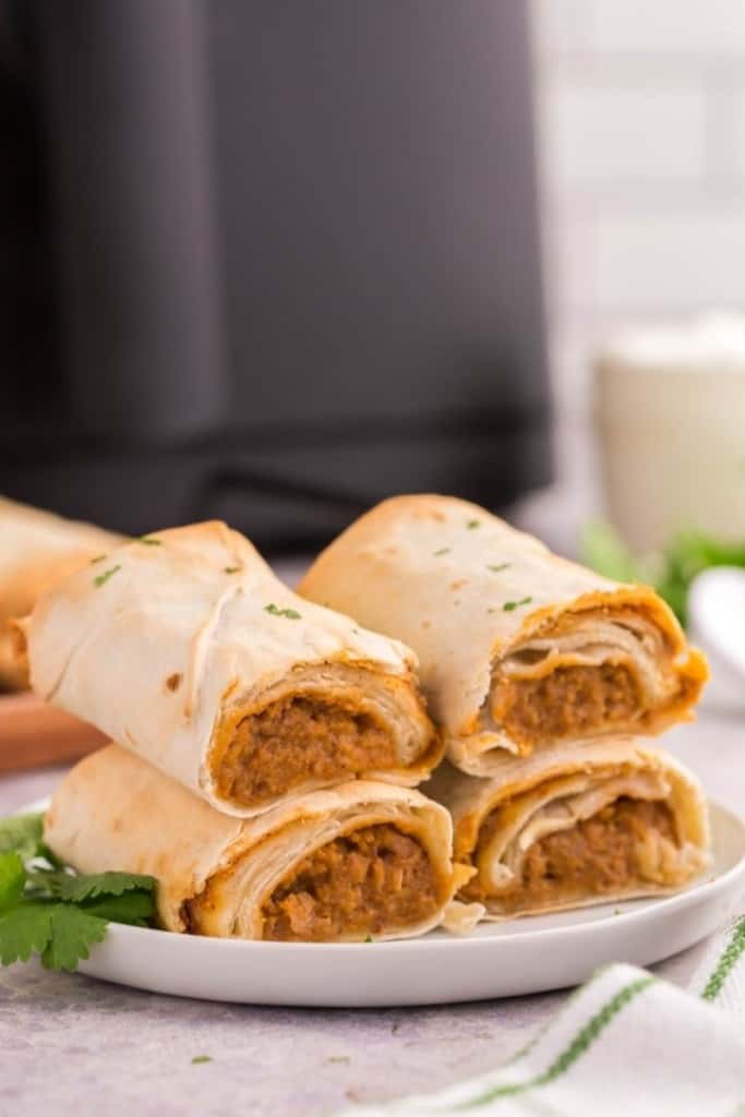 Two burritos halved and stacked on top of each other on a white plate and air fryer in the background