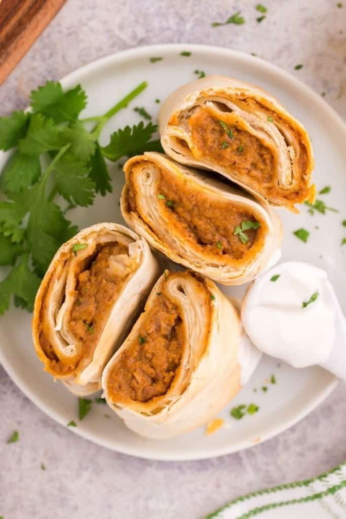 Frozen burritos cut in half on a white plate with sour cream and cilantro plated with it
