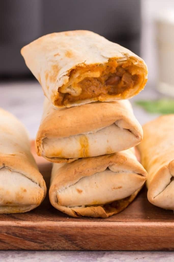 Cooked frozen burritos stacked on top of each other on a wooden serving platter