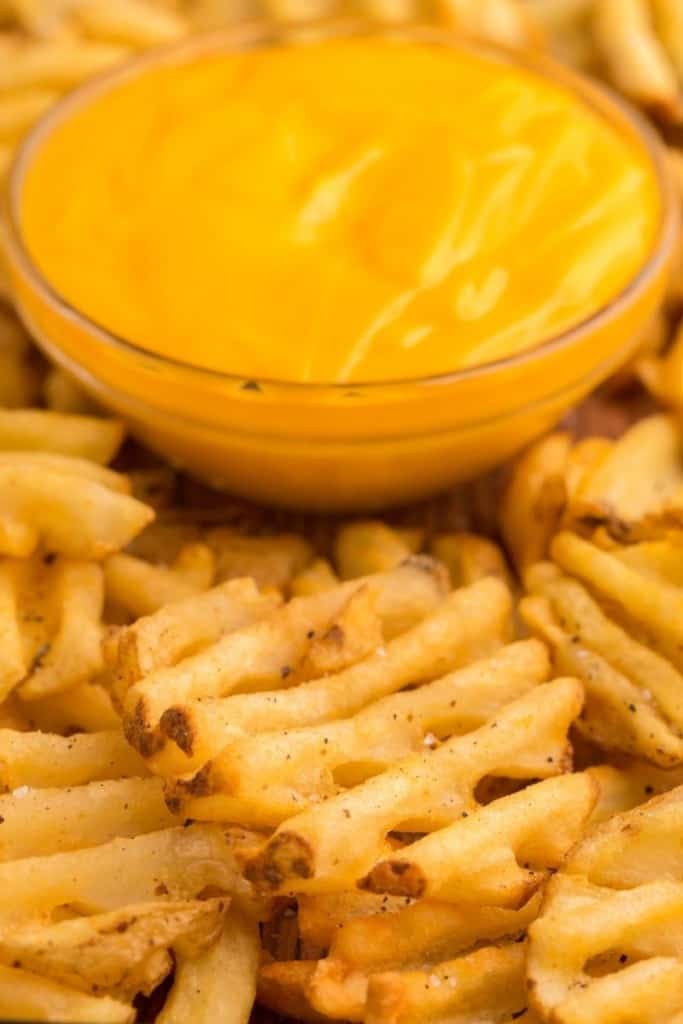 Closeup of cooked air fried waffle fries and bowl of nacho cheese