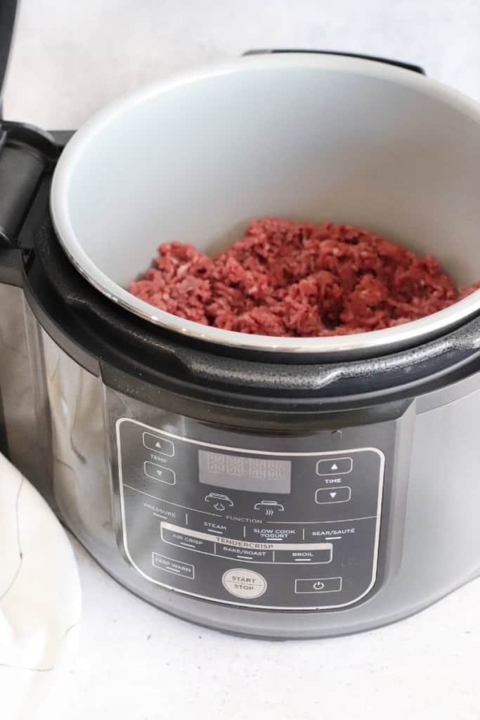 Raw ground beef being sauteed in the Ninja Foodi