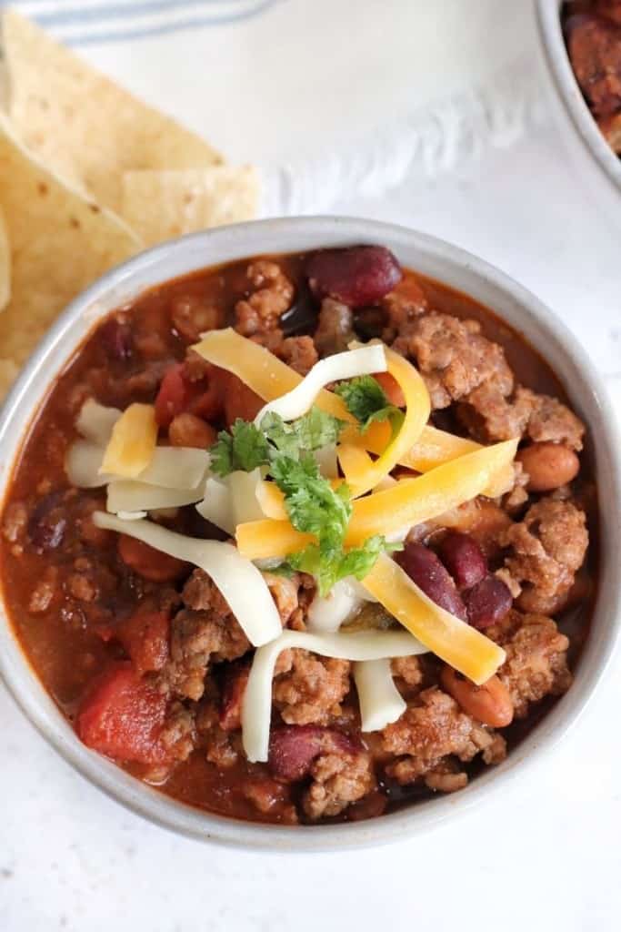 Closeup of Ninja Foodi chili recipe in a bowl topped with shredded cheese and cilantro with tortilla chips to the side
