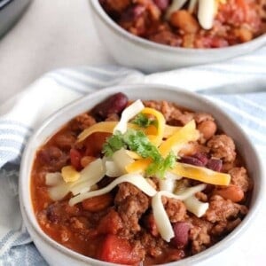 Closeup of a bowl of chili topped with shredded cheese and some cilantro
