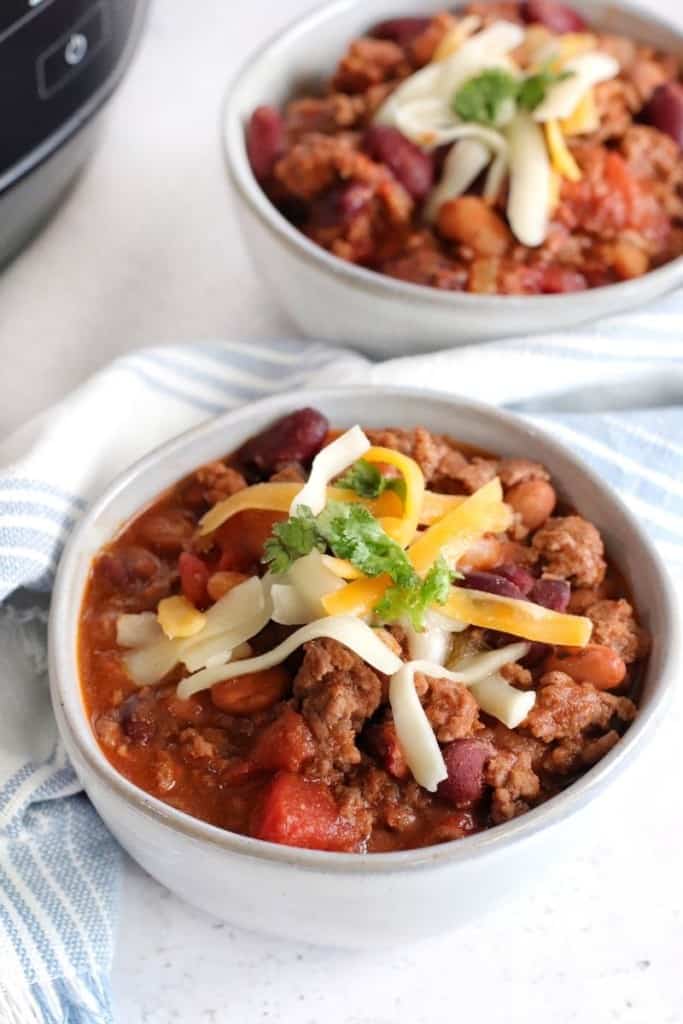 Closeup of a bowl of chili topped with shredded cheese and some cilantro