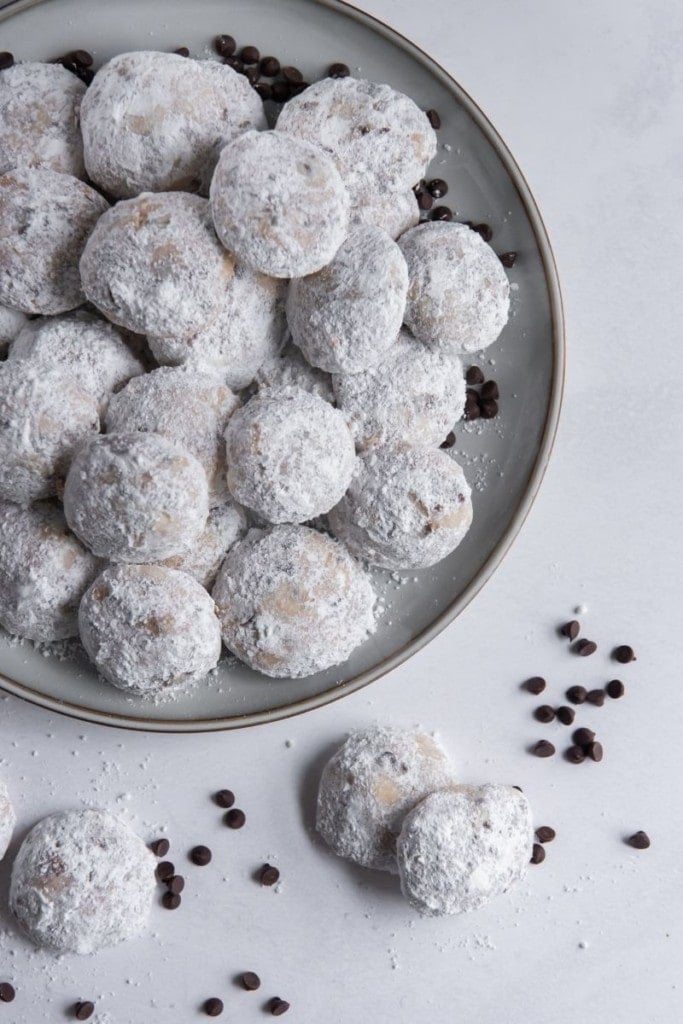 Snowball Cookies with no nuts on a grey round plate and some chocolate chips around it