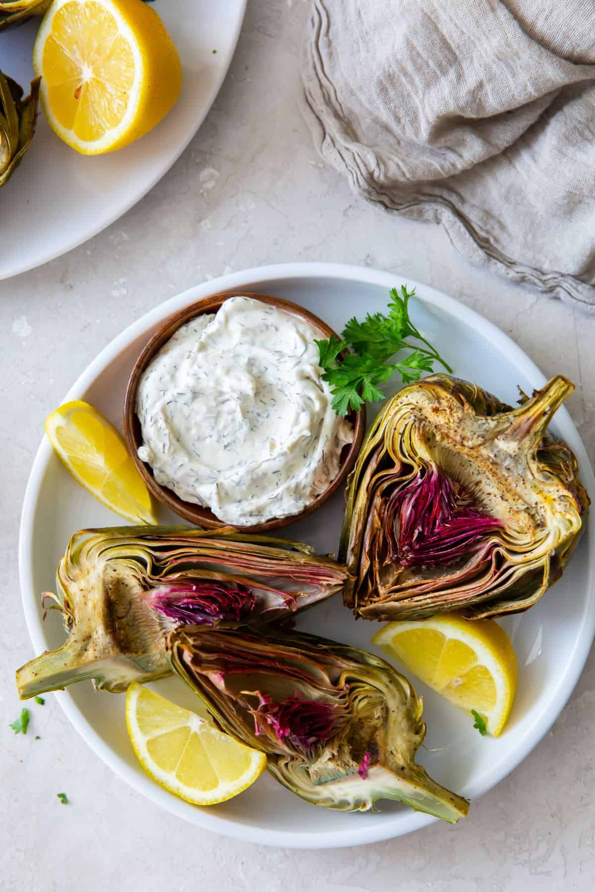 Air fryer artichokes on a plate with dip and lemon.