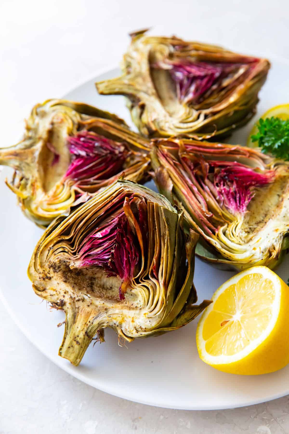 Two artichokes cut in half served on a plate with lemon.