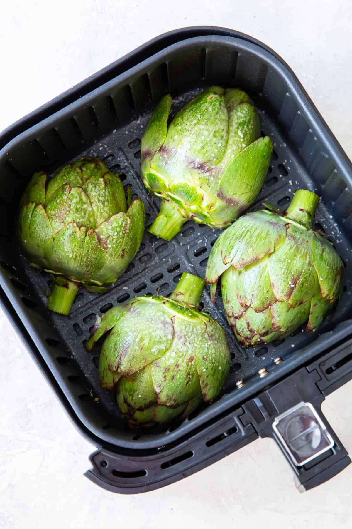 Artichokes in the air fryer basket with cut side down.