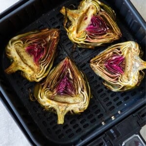 Artichokes in the air fryer basket cut side up.