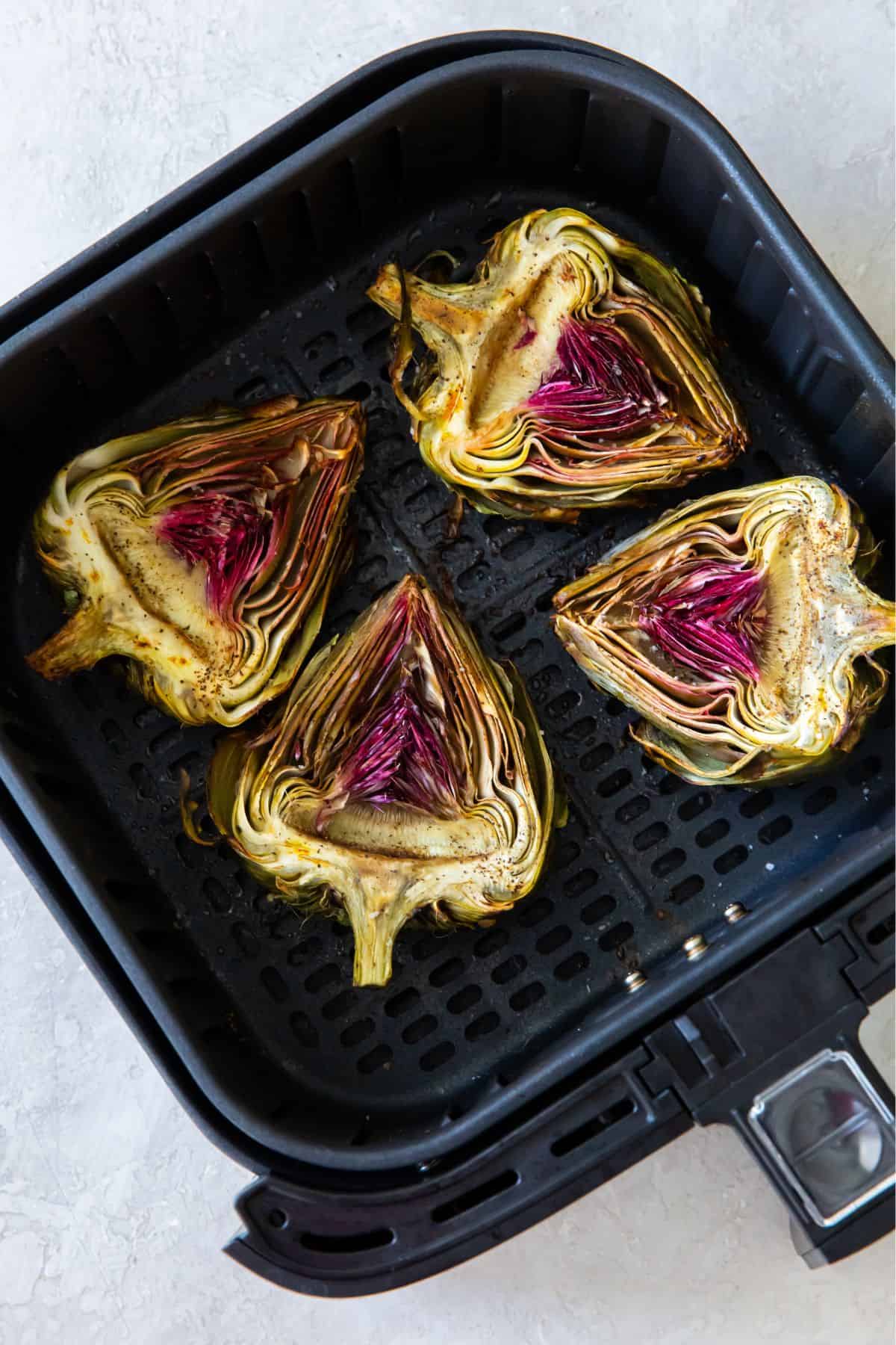 Artichokes in the air fryer basket cut side up.