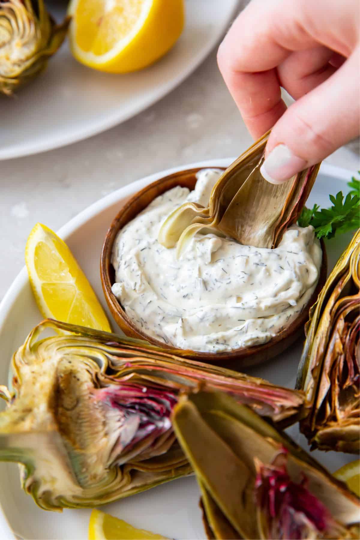 Air fryer artichoke piece being dipped into a white dip.