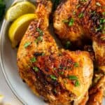 Close up of air fried chicken leg quarters on a white plate served next to lemon slices.