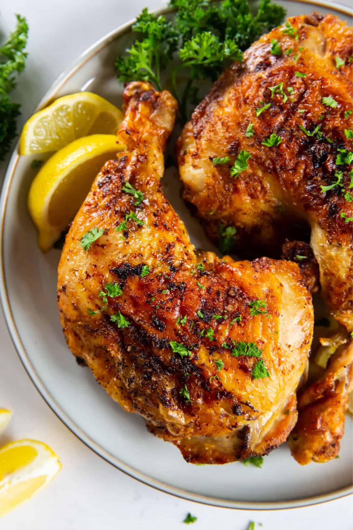 Close up of air fried chicken leg quarters on a white plate served next to lemon slices.