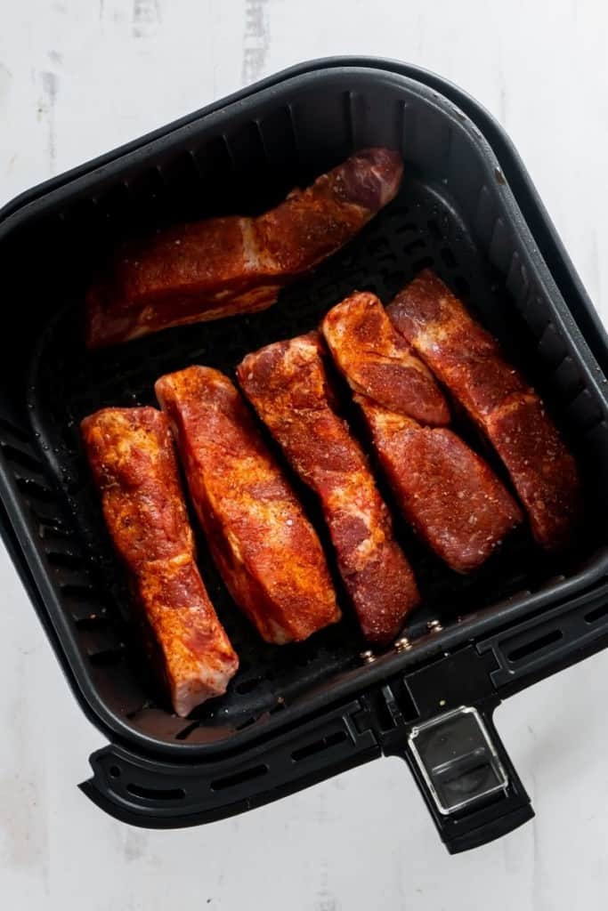 Raw country style pork ribs in an air fryer basket.