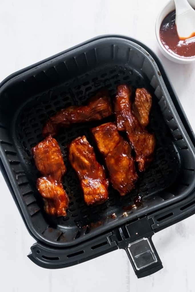 Halfway cooked ribs in an air fryer basket with BBQ sauce basted on.
