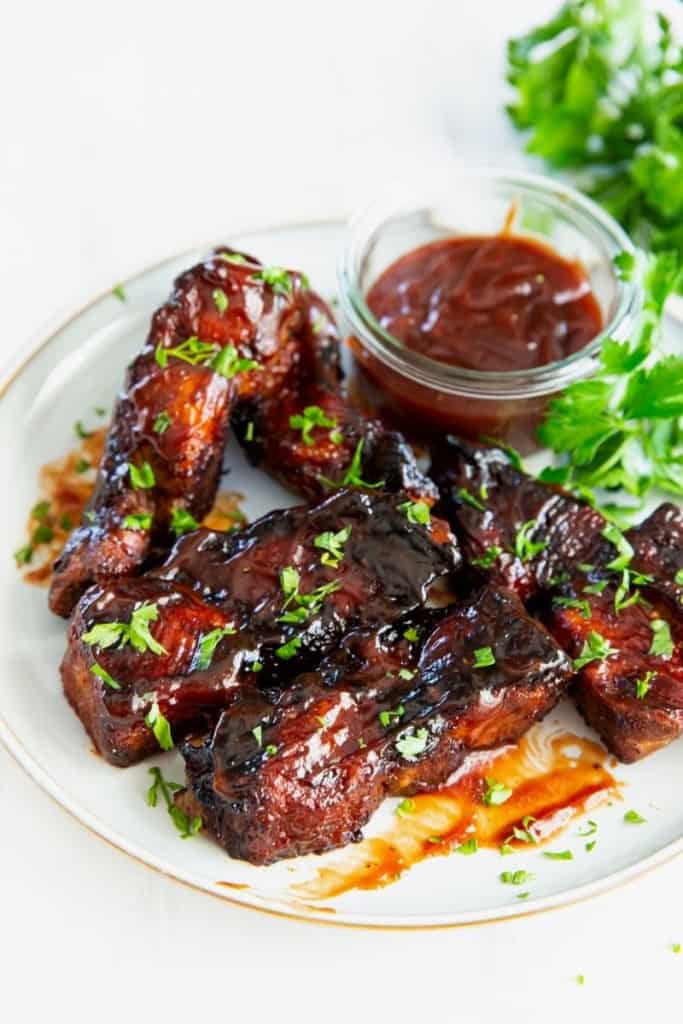 Air fryer country style ribs coated with BBQ sauce on a white plate.
