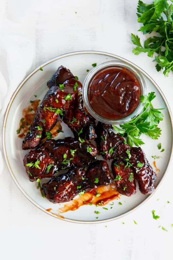 Overhead view of country style ribs on a white plate with BBQ sauce.