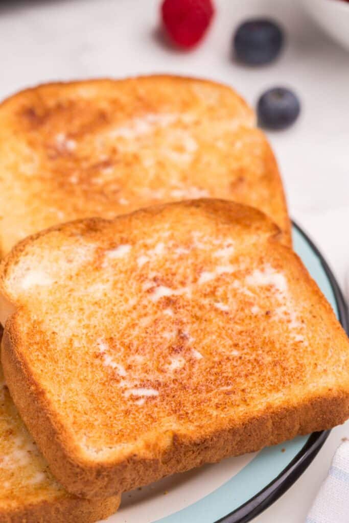 Close up of a piece of golden brown air fryer toast with melted butter on it.