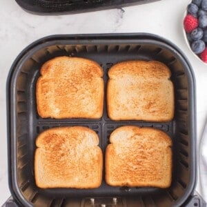 4 pieces of toast in an air fryer basket with perfect golden brown on top.