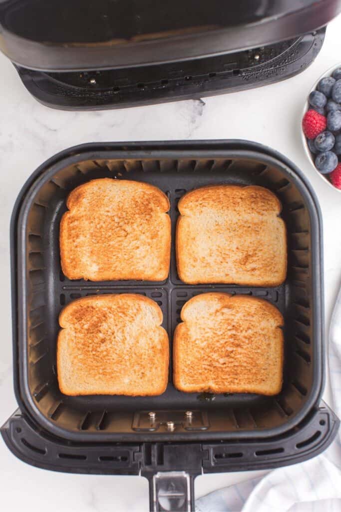 4 pieces of toast in an air fryer basket with perfect golden brown on top.