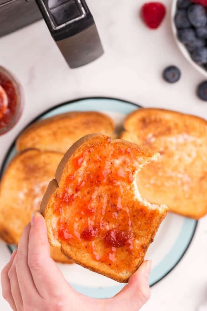 Air fryer toast with jam on top with a bite taken out of it being held in a hand.