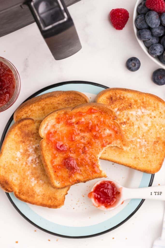 Air fryer toast on a plate with jam on top with a bite taken out of it.
