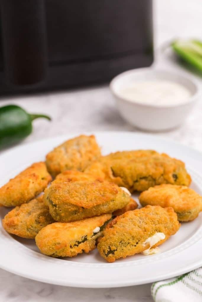 pile of jalapeno poppers on white plate with dipping sauce