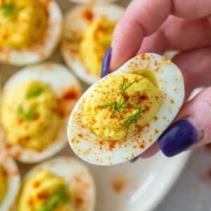 Hand grabbing a deviled egg without vinegar from plate